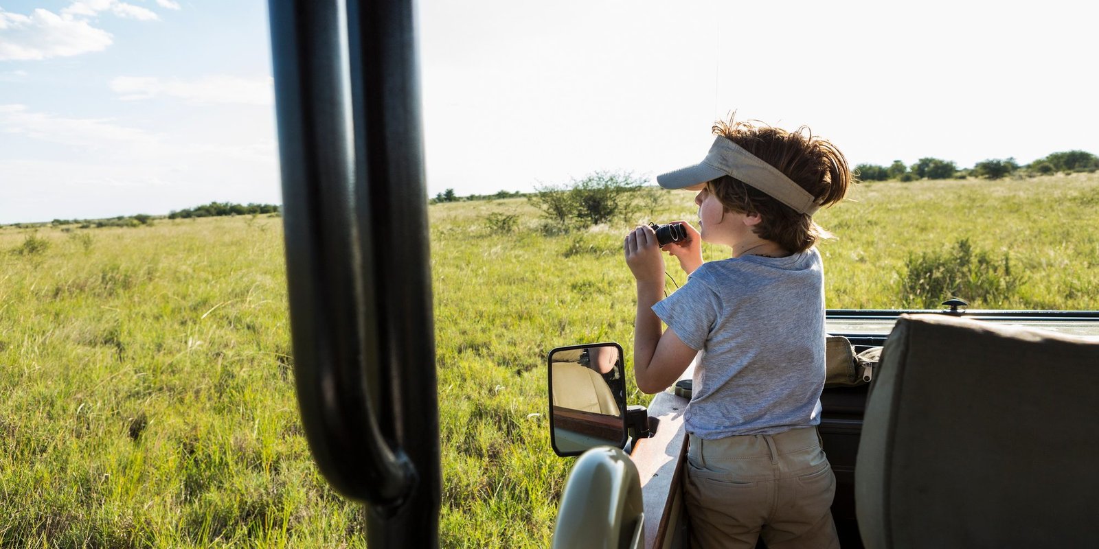 A six year old boy with binoculars in a safari vehicle